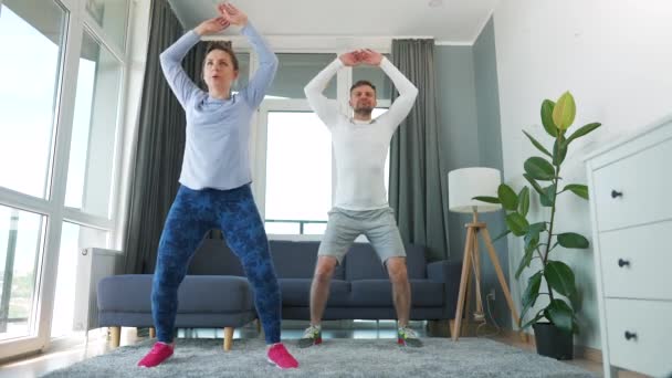 Caucasian couple is doing jumping jacks exercise at home in cozy bright room, slow motion. — Stock Video