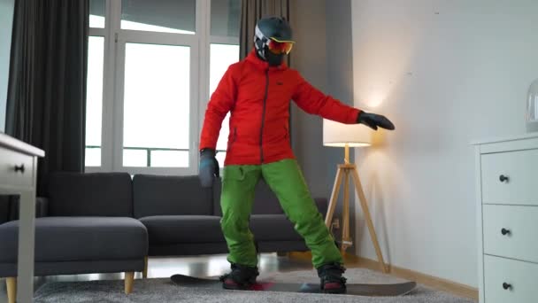 Забавное видео. Человек, одетый сноубордистом, изображает сноубординг на ковре в уютной комнате. В ожидании снежной зимы. — стоковое видео
