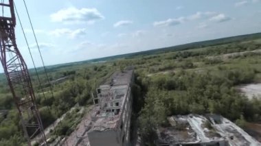 FPV insansız hava aracı, terk edilmiş sanayi binaları ve bir kazıcının etrafında hızla ve manevra kabiliyetiyle uçar..