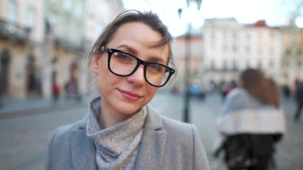 Portrait d'une femme caucasienne avec des lunettes debout au milieu de la place de la vieille ville. Elle regarde sérieusement la caméra. Mouvement lent — Video