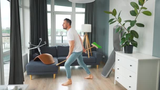 Hombre limpiando la casa y divirtiéndose bailando con una escoba. Movimiento lento — Vídeo de stock