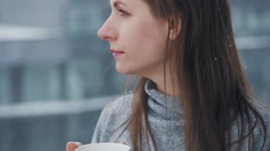 Beyaz kadın kar yağışı sırasında sıcak kahve ya da çayla balkonda kalır. Kar tanelerine bakıyor ve soğuk temiz havayı soluyor.