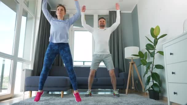 Caucásico pareja está haciendo saltar gatos ejercicio en casa en acogedor habitación luminosa. — Vídeos de Stock