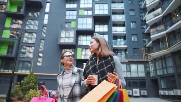 Δύο ευτυχισμένες γυναίκες περπατούν με τσάντες για ψώνια και παίρνουν καφέ μετά από επιτυχημένα ψώνια και μιλάνε με ενδιαφέρον μεταξύ τους.. — Αρχείο Βίντεο