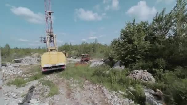 El dron FPV vuela rápido y maniobrable entre edificios industriales abandonados y alrededor de una excavadora. — Vídeos de Stock