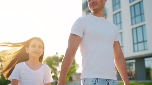 Pa en dochter lopen rond bij zonsondergang. Kind houdt vaders hand vast. Langzame beweging — Stockvideo