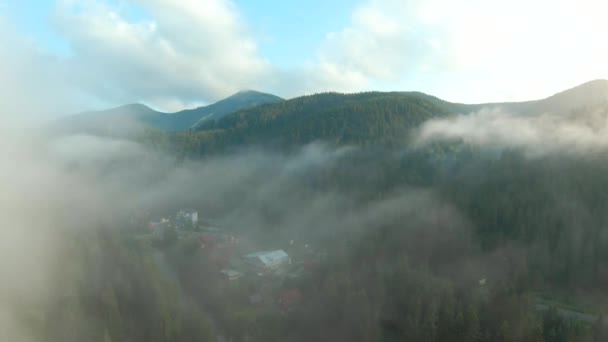 Vlucht over een bergresort tussen het naaldbos. Mist stijgt over de berghellingen — Stockvideo