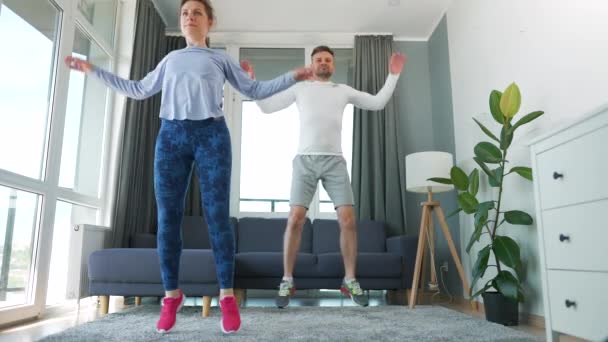 Kaukasisch paar doet jumpingjacks oefening thuis in gezellige lichte kamer, slow motion. — Stockvideo