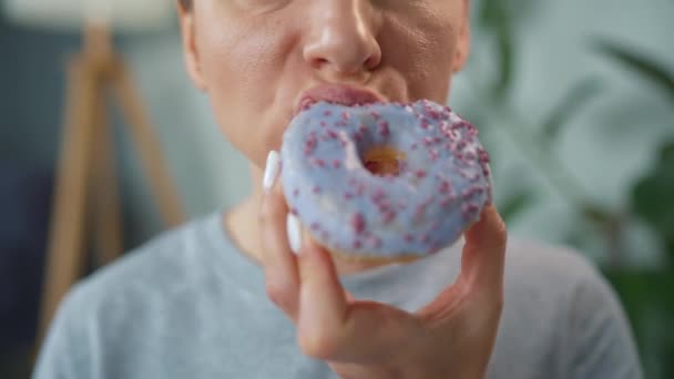 Mujer comiendo una rosquilla dulce en esmalte púrpura con salpicaduras. Primer plano — Vídeos de Stock