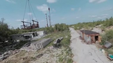 FPV insansız hava aracı, terk edilmiş sanayi binaları ve bir kazıcının etrafında hızla ve manevra kabiliyetiyle uçar..