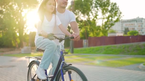 Pappa lär dottern cykla i solnedgången. Långsamma rörelser — Stockvideo