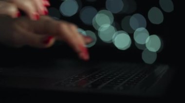Kadın eller geceleri dizüstü bilgisayarda yazıyorlar. Arkaplanda bulanık ışıklar