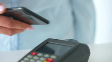 Akıllı telefondan yapılan temassız ödeme. Kablosuz ödeme konsepti. Yakın plan, kadın banka terminalindeki siparişi ödemek için akıllı telefon nakitsiz cüzdan teknolojisi kullanıyor..