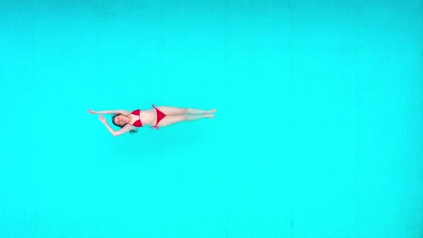 从上往下看，就像一个穿着红色泳衣的女人躺在游泳池里。放松的概念 — 图库视频影像