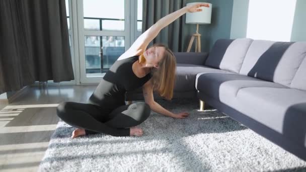 Junge kaukasische Frau im schwarzen Overall macht Yoga zu Hause, um Flexibilität und Gleichgewicht zu entwickeln. — Stockvideo