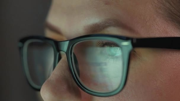 Frau mit Brille blickt auf den Monitor und arbeitet mit Diagrammen und Analysen. Der Monitor-Bildschirm spiegelt sich in der Brille wider. Arbeiten in der Nacht. Extreme Nahaufnahme — Stockvideo