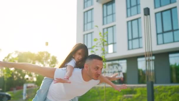 Liebender Papa spielt Huckepack-Tochter. Vater, der kleines Mädchen auf dem Rücken trägt, tut so, als ob er fliegen würde, und träumt vom gemeinsamen Urlaub im Freien. Zeitlupe — Stockvideo