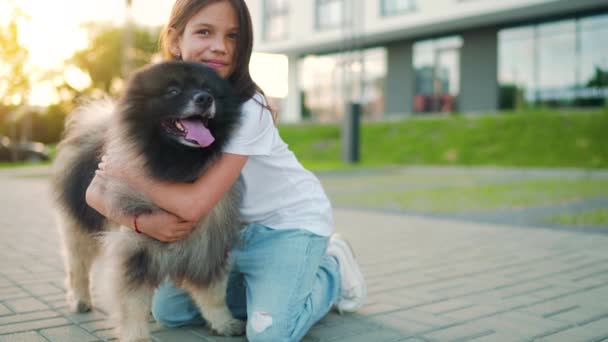 Esmer kız gün batımında pofuduk bir köpeğe sarılır. Yavaş çekim — Stok video