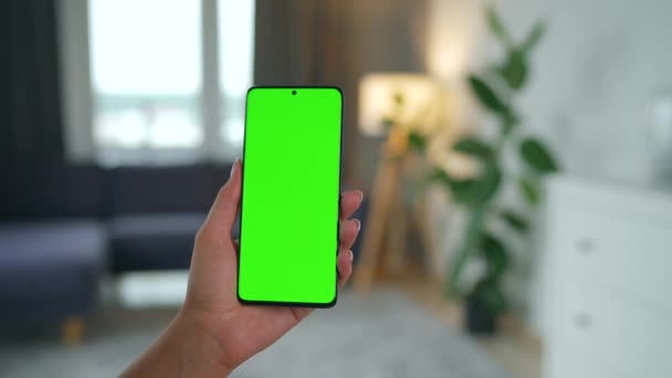 Mujer en casa usando smartphone con pantalla verde en modo vertical. Chica navegando por Internet, viendo contenido, videos. POV. — Vídeo de stock