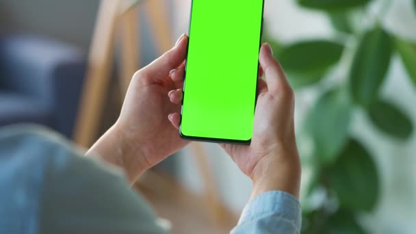 Mujer en casa usando smartphone con pantalla verde en modo vertical. Chica navegando por Internet, viendo contenido, videos. POV. — Vídeos de Stock