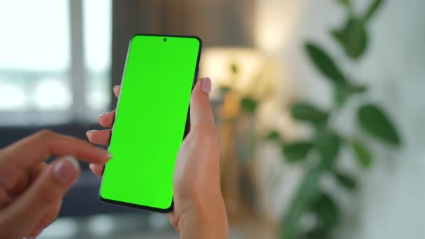 Woman at home using smartphone with green mock-up screen in vertical mode. Girl browsing Internet, watching content, videos. POV. — Stock Video