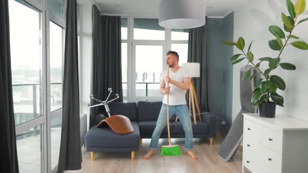 Hombre limpiando la casa y divirtiéndose bailando y cantando con una escoba. Movimiento lento — Vídeo de stock