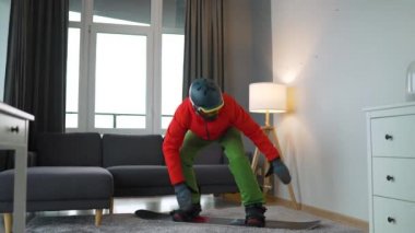 Komik video. Snowboard sporcusu gibi giyinmiş bir adam rahat bir odada halının üzerinde snowboard yaparken resmediyor. Karlı bir kış bekliyor. Yavaş çekim