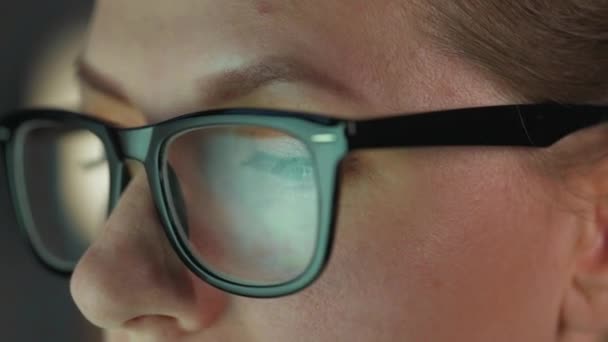 Woman in glasses looking on the monitor and and working with charts and analytics. The monitor screen is reflected in the glasses. Work at night. Extreme close-up — Stock Video