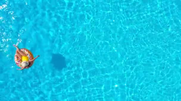 Luftaufnahme einer Frau im gelben Badeanzug, die auf einem Donut im Pool liegt — Stockvideo