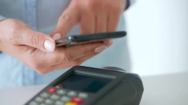 Akıllı telefondan yapılan temassız ödeme. Kablosuz ödeme konsepti. Yakın plan, kadın banka terminalindeki siparişi ödemek için akıllı telefon nakitsiz cüzdan teknolojisi kullanıyor..