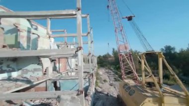 FPV insansız hava aracı, terk edilmiş sanayi binaları ve bir kazıcının etrafında hızla ve manevra kabiliyetiyle uçar..