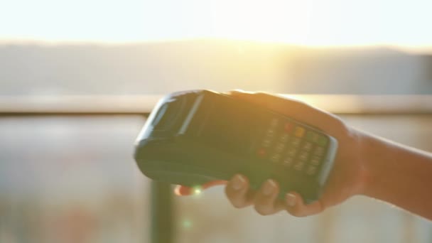 Close-up, man using smartphone cashless wallet NFC technology to pay order on bank terminal. Card machine in female hand on sunlight background — Stock Video