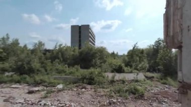 FPV insansız hava aracı, terk edilmiş sanayi binaları ve bir kazıcının etrafında hızla ve manevra kabiliyetiyle uçar..