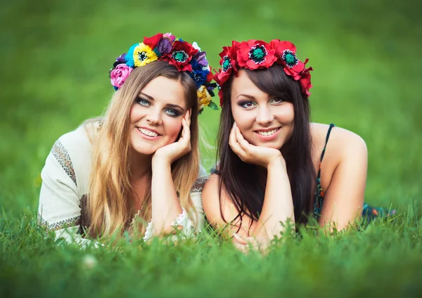 Two laughing girl in Ukrainian national costumes lie on the gree — Stock Photo, Image