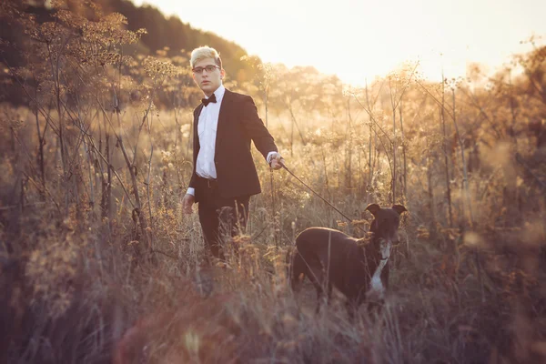 Joven hombre atractivo en traje y corbata con un perro galgo en aut — Foto de Stock