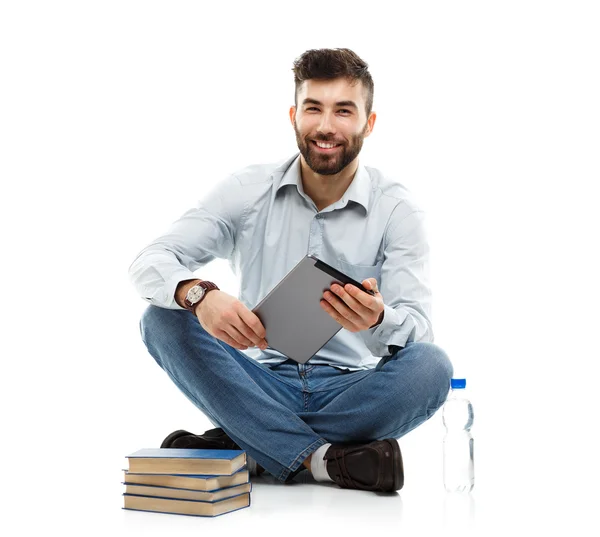 Joven barbudo sonriente sosteniendo una tableta con libros y un bott —  Fotos de Stock