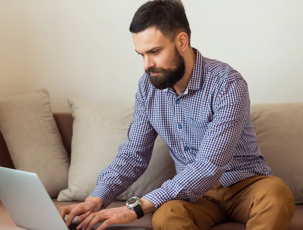 Jeune homme barbu travaillant sur ordinateur portable à la maison — Photo