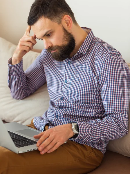 Young bearded man working on laptop at home — Stock Photo, Image