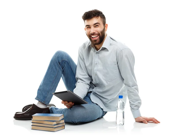 Joven barbudo sonriente sosteniendo una tableta con libros y un bott —  Fotos de Stock