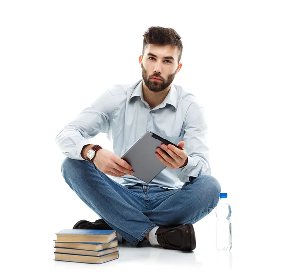 Joven barbudo sonriente sosteniendo una tableta con libros y un bott —  Fotos de Stock