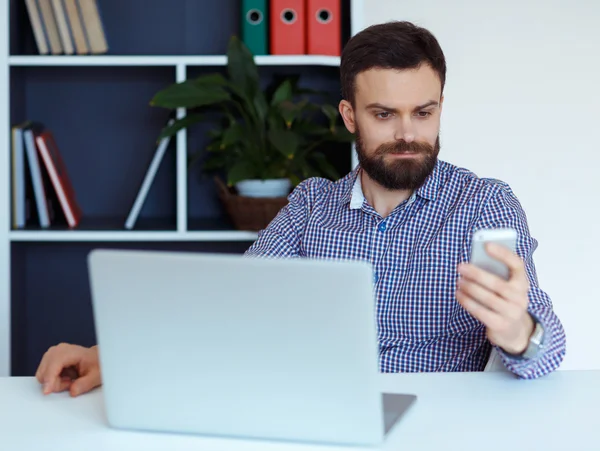 Homme barbu travaillant sur un ordinateur portable dans le bureau et parlant sur le colis — Photo