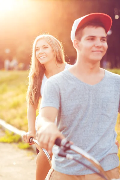 Young man and woman riding a bicycle in the park outdoors — Stock Photo, Image