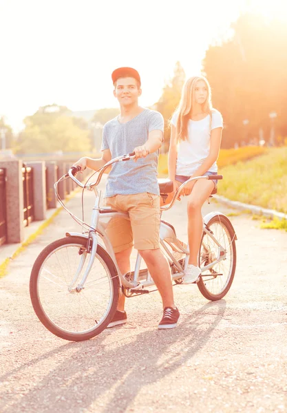 Young man and woman riding a bicycle in the park outdoors — Stock Photo, Image