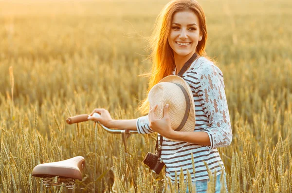 Wanita muda yang cantik berdiri di lapangan dengan sepedanya — Stok Foto