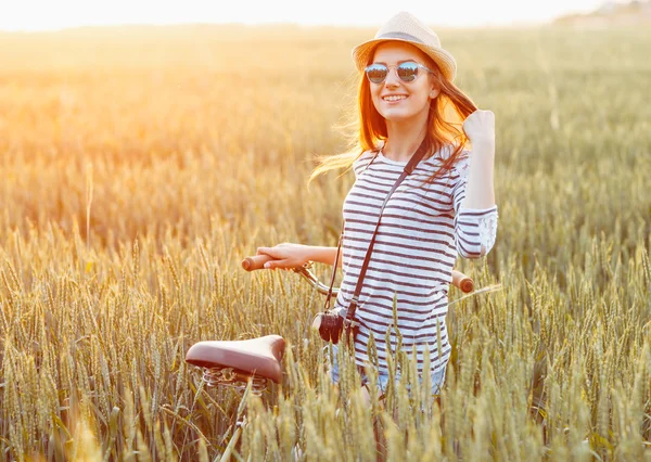 Lovely young woman stands in a field with her bicycle — Stock Photo, Image