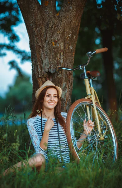Härlig ung kvinna i en hatt med en cykel utomhus — Stockfoto