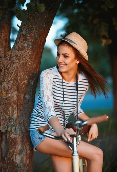 Linda jovem mulher em um chapéu com uma bicicleta ao ar livre — Fotografia de Stock