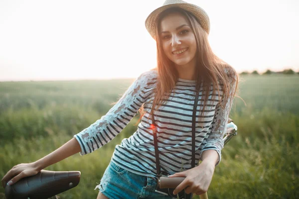 Lovely young woman stands in a field with her bicycle — Stock Photo, Image