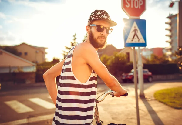 Stylish man in sunglasses riding a bicycle on a city street at s — Stock Photo, Image