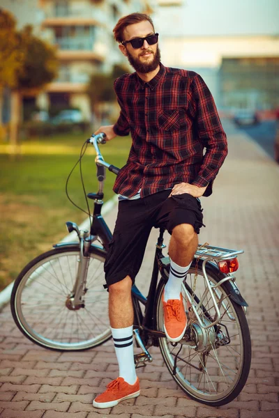 Stylish man in sunglasses riding a bike on city street — Stock Photo, Image